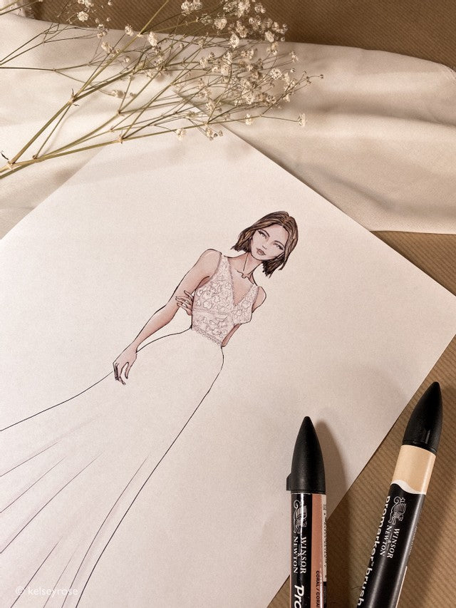 A sketch drawing of a woman wearing a Kelsey Rose wedding dress with two pencils laying over the sketch 